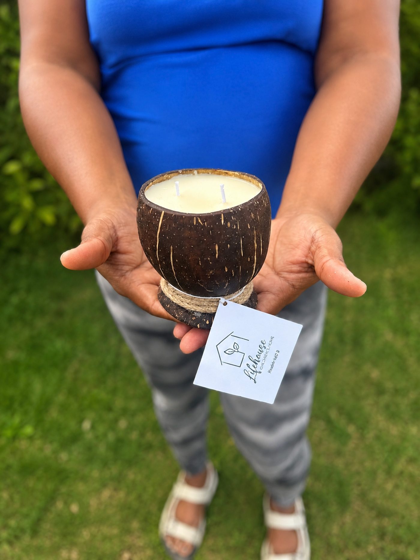 A two-wick candle poured into a rope-wrapped coconut shell, held in two open hands