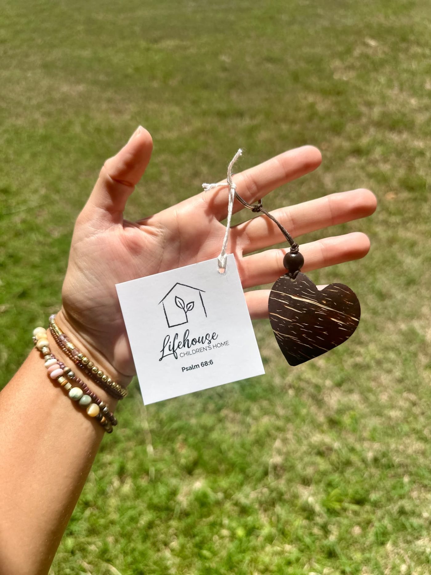An open palm holding a coconut shell heart keychain with a Lifehouse Children's Home hangtag